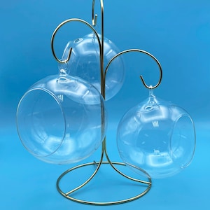 Può includere: Un supporto in metallo dorato con tre sfere di vetro appese. Le sfere sono trasparenti e rotonde.