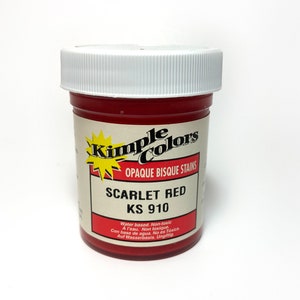 Puede incluir: Un frasco cilíndrico de plástico de Kimple Colors Opaque Bisque Stains en Scarlet Red, modelo KS 910. El recipiente cuenta con una tapa blanca de rosca y una etiqueta con el nombre de la marca, el color, el número de modelo y texto de seguridad.