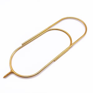 May include: A gold-colored metal paperclip-shaped object with a screw at the bottom. The paperclip has a rounded oval shape with a straight line extending from the top. The screw is a small, gold-colored metal piece.
