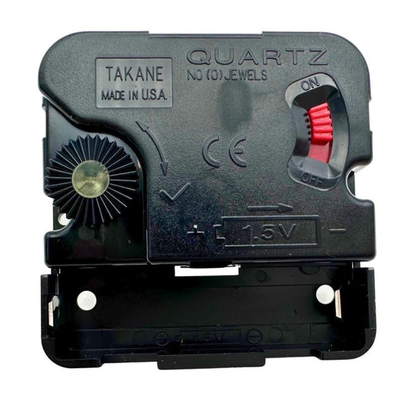 K&ouml;nnte beinhalten: Schwarzes Quarz-Uhrwerk mit rotem Ein-/Ausschalter. Der Uhrenmechanismus tr&auml;gt die Aufschrift "TAKANE MADE IN U.S.A." und "QUARTZ NO (0) JEWELS". Es hat auch ein Batteriefach f&uuml;r eine 1,5-V-Batterie.