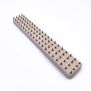 May include: A long, rectangular, beige-colored tool with black, pointed spikes evenly spaced across the surface.