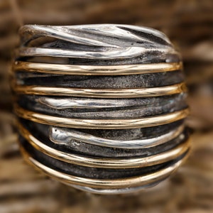 May include: A silver and gold ring with a woven design. The ring is made of multiple strands of metal that are twisted and intertwined.