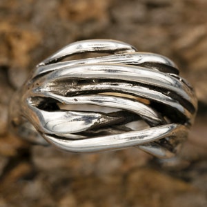 May include: A silver ring with a unique, organic design. The ring is made of multiple strands of silver that are twisted and intertwined to create a textured, abstract look.