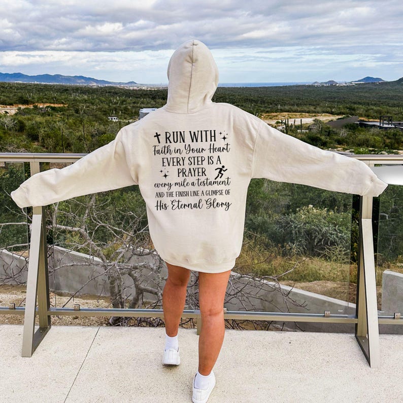 May include: A beige hoodie with a black print that reads "RUN WITH Faith in Your Heart EVERY STEP IS A PRAYER every mile a testament AND THE FINISH LINE A GLIMPSE OF His Eternal Glory".