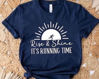 May include: Navy blue t-shirt with a white graphic of a sunrise with a running person and the text "Rise & Shine It's Running Time".