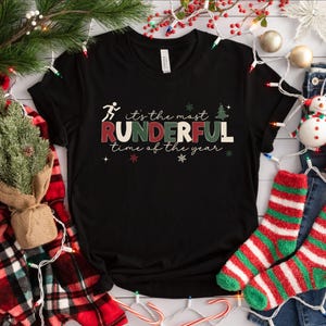 May include: Black t-shirt with a red, green, and white graphic that says "it's the most RUNDERFUL time of the year". A running person icon is above the text.