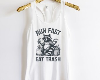 May include: White tank top with a black and white illustration of a raccoon eating tacos and sitting in a trash can. The text "Run Fast Eat Trash" is printed on the shirt.