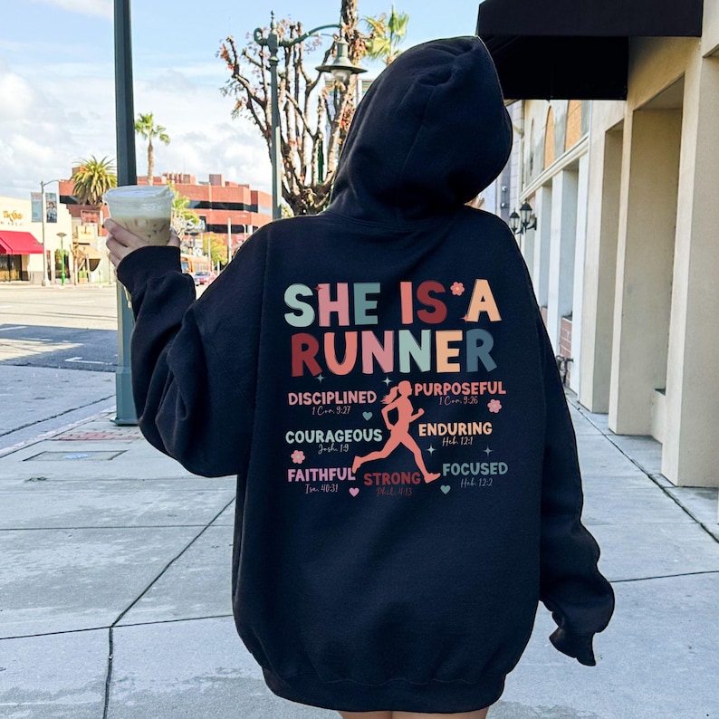 May include: Black hoodie with a graphic print that says "She is a Runner" with a running woman silhouette and bible verses.
