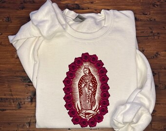 May include: White sweatshirt with a red and white image of the Virgin Mary surrounded by a wreath of pink roses.