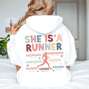 May include: White hoodie with the text "She is a Runner" in colorful letters. The text is surrounded by a design of running figures and inspirational words with bible verses.