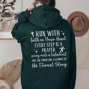 May include: A dark green hooded sweatshirt with a white graphic print that reads "RUN WITH Faith in Your Heart EVERY STEP IS A PRAYER every mile a testament AND THE FINISH LINE A GLIMPSE OF His Eternal Glory".