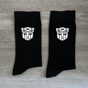 May include: A pair of black socks with a white Transformers logo on each sock.