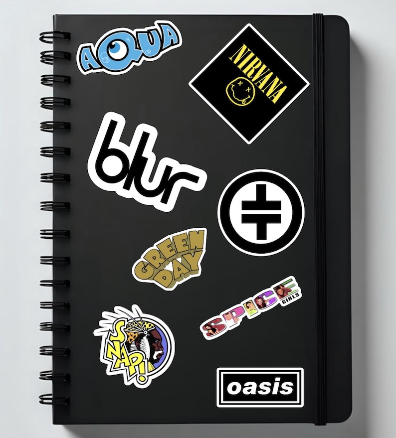 May include: Black notebook with spiral binding, featuring stickers of the bands Aqua, Blur, Green Day, Nirvana, Spice Girls, Snap!, Oasis, and a black and white symbol. The stickers are in various colors and designs.