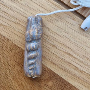 May include: A handcrafted, light blue and brown ceramic light pull with a textured, carved design. The pull is attached to a white cord and a white plastic connector. The pull is approximately 7.6 cm long.