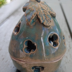 May include: A ceramic incense burner with a leaf design on top. The burner is teal and brown with a glazed finish and has multiple holes around the sides.