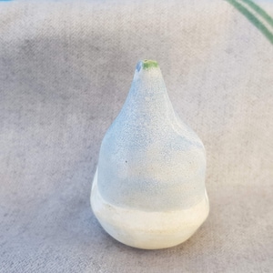 May include: A small, light blue ceramic vase with a white base. The vase has a rounded, teardrop shape and a small opening at the top.