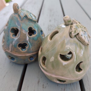 May include: Two ceramic candle holders shaped like figs with intricate cutouts. One is green and the other is blue and green.