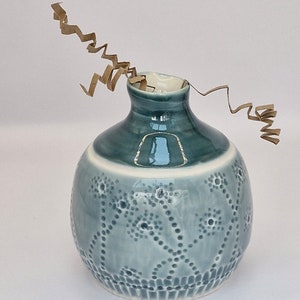 May include: A small, round, blue ceramic vase with a white rim and a textured design. The vase has a narrow neck and a wide base.