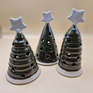 May include: Three ceramic Christmas tree candle holders with white star toppers. The trees are green with a brown glaze and have holes for tea lights.