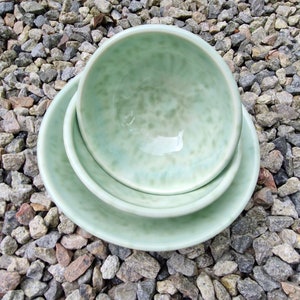May include: Three green ceramic bowls stacked on top of each other. The bowls have a speckled glaze and are nested together.
