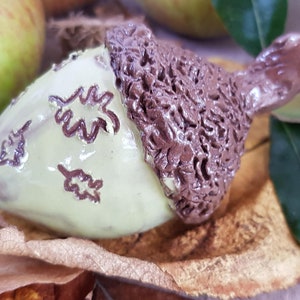 May include: A ceramic acorn ornament with a brown cap and a light green body decorated with brown leaf designs.