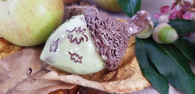 May include: A ceramic acorn ornament with a brown cap and a light green body decorated with brown leaf designs.