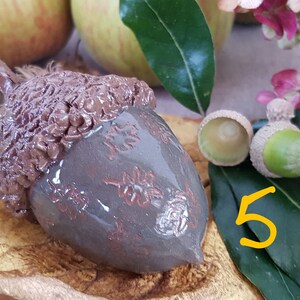 May include: A ceramic acorn ornament with a brown and grey glaze. The acorn is decorated with a leaf pattern and has a textured cap.