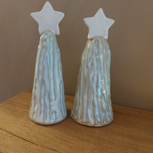 May include: Two white ceramic Christmas trees with a star on top. The trees are textured to look like wood.