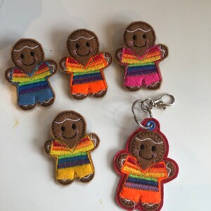 May include: Five gingerbread person ornaments with rainbow striped shirts. One gingerbread person is attached to a silver key chain.