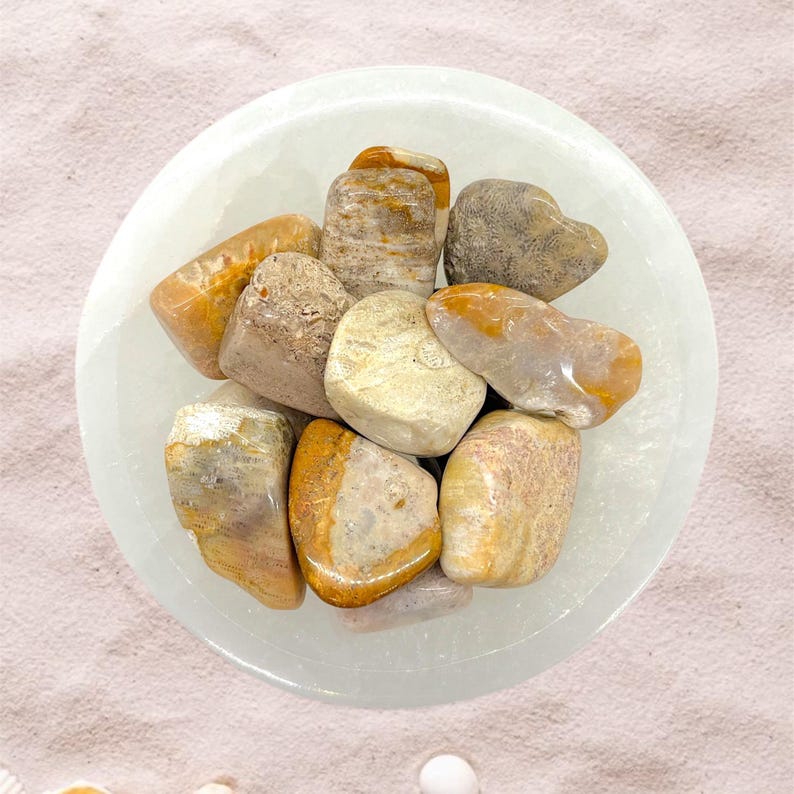 Peut inclure: Un ensemble de pierres polies aux tons de beige, marron et orange, nich&eacute;es dans un bol blanc peu profond. Les pierres varient en taille et en forme, avec des surfaces lisses et arrondies. Le bol repose sur une surface rose clair.