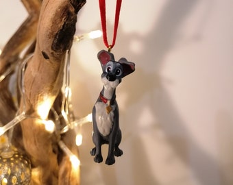 May include: A gray and white dog figurine with a red collar and a gold tag hanging from the collar. The figurine is hanging from a red ribbon.
