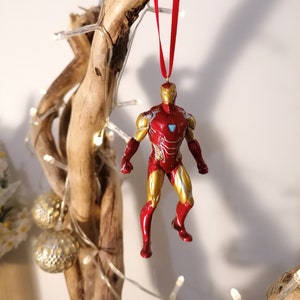 May include: Red and gold Iron Man Christmas ornament hanging from a branch with white lights.