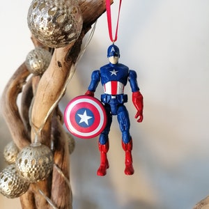 May include: A red, white, and blue Captain America action figure ornament with a red ribbon and a silver star on his shield.