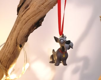 May include: A gray and white dog ornament with a red collar and a gold tag hanging from a red ribbon. The ornament is hanging from a branch.