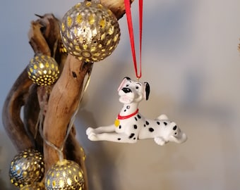 May include: A white and black Dalmatian dog Christmas ornament hanging from a branch with a red ribbon. The ornament is surrounded by gold, decorative, light-up ornaments.