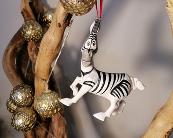 May include: A white and black zebra figurine ornament hanging from a branch with gold and white ornaments. The zebra is in a running pose with its mouth open and its eyes wide.