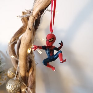 May include: A red and blue Spider-Man Christmas ornament hanging from a driftwood branch with white Christmas lights.
