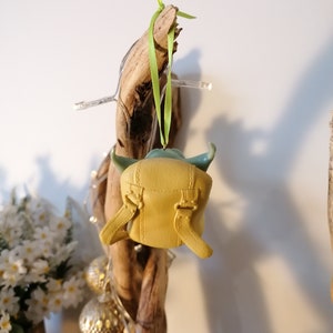 May include: A green and yellow Yoda ornament hanging from a piece of driftwood with a green ribbon.