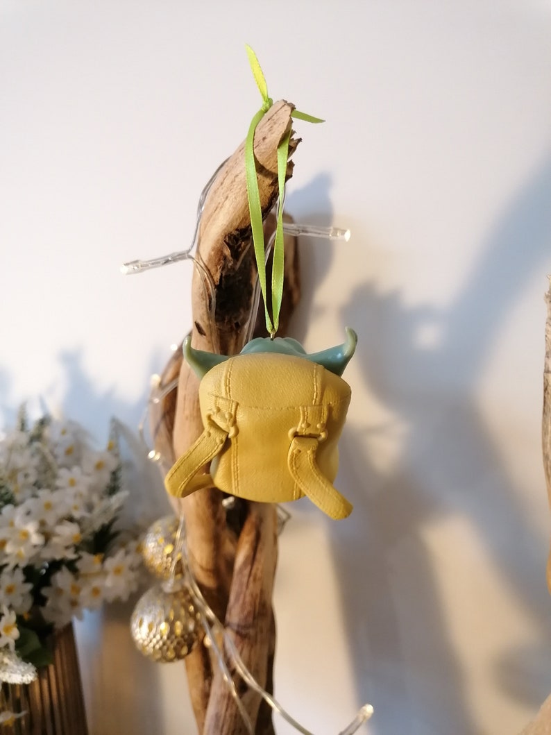 May include: A green and yellow Yoda ornament hanging from a piece of driftwood with a green ribbon.