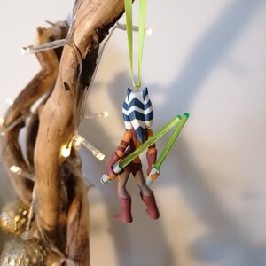 May include: A green and blue Star Wars character ornament with two green lightsabers. The ornament is hanging from a green ribbon.