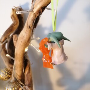 May include: Green and orange Christmas bauble featuring a character from the Star Wars franchise. The bauble is hanging from a green ribbon.