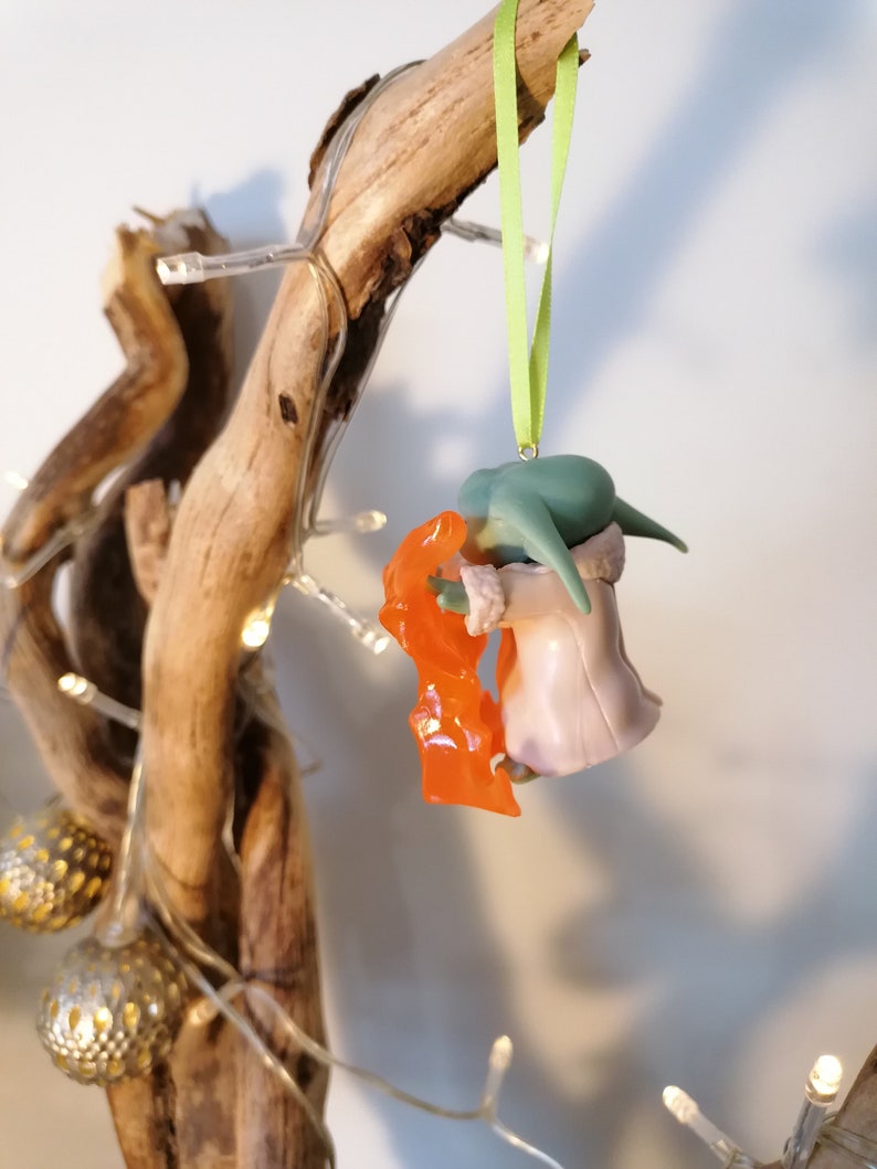 May include: Green and orange Christmas bauble featuring a character from the Star Wars franchise. The bauble is hanging from a green ribbon.