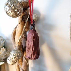 May include: A brown and black Christmas ornament shaped like a character from Star Wars. The ornament is hanging from a red ribbon.