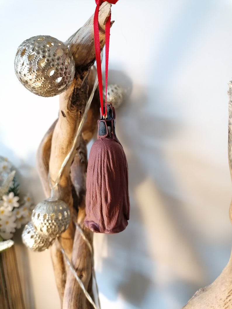 May include: A brown and black Christmas ornament shaped like a character from Star Wars. The ornament is hanging from a red ribbon.