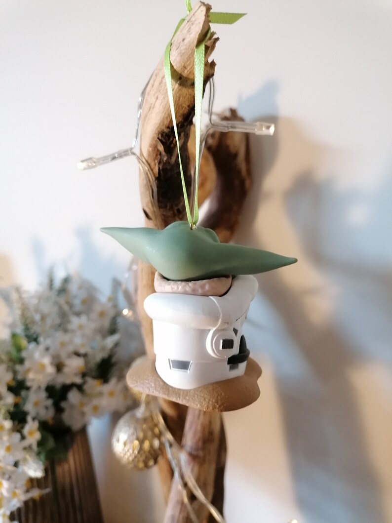 K&ouml;nnte beinhalten: Ein gr&uuml;ner und wei&szlig;er Weihnachtsbaumschmuck mit einer Figur aus dem Star Wars-Franchise. Der Schmuck h&auml;ngt an einem St&uuml;ck Treibholz.