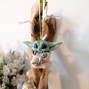 May include: A green and pink handmade ornament of a popular character from the Star Wars franchise. The ornament is hanging from a green ribbon.