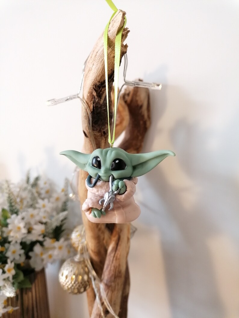 May include: A green and pink handmade ornament of a popular character from the Star Wars franchise. The ornament is hanging from a green ribbon.