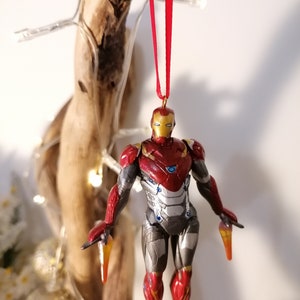 May include: Red and gold Iron Man Christmas ornament with a red ribbon. The ornament is a detailed figurine of Iron Man in flight.