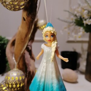 Peut inclure: Une poup&eacute;e en plastique bleue et blanche avec des cheveux blonds portant une robe bleue et blanche. La poup&eacute;e est suspendue &agrave; une ficelle blanche.