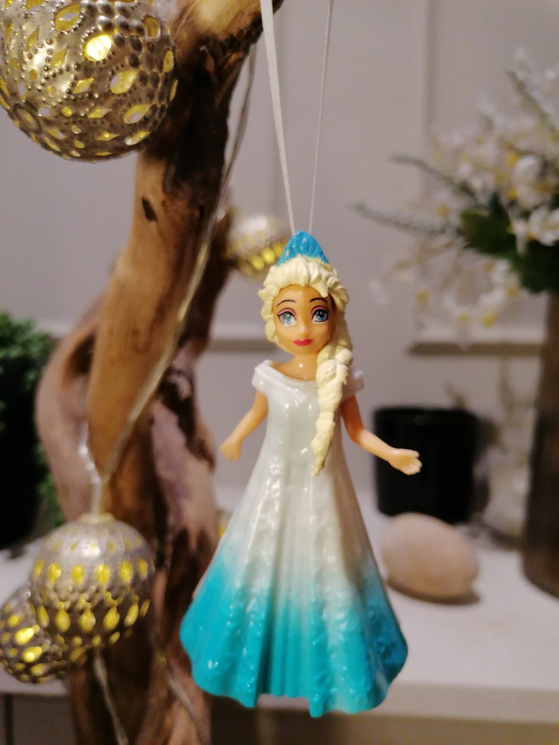 Peut inclure: Une poup&eacute;e en plastique bleue et blanche avec des cheveux blonds portant une robe bleue et blanche. La poup&eacute;e est suspendue &agrave; une ficelle blanche.